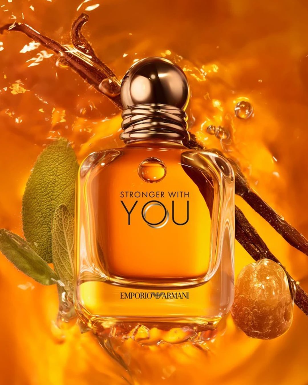 Das goldfarbene Parfüm „Stronger With You“ von Emporio Armani liegt in einer goldenen Flüssigkeit, umgeben von Blättern und Zweigen.