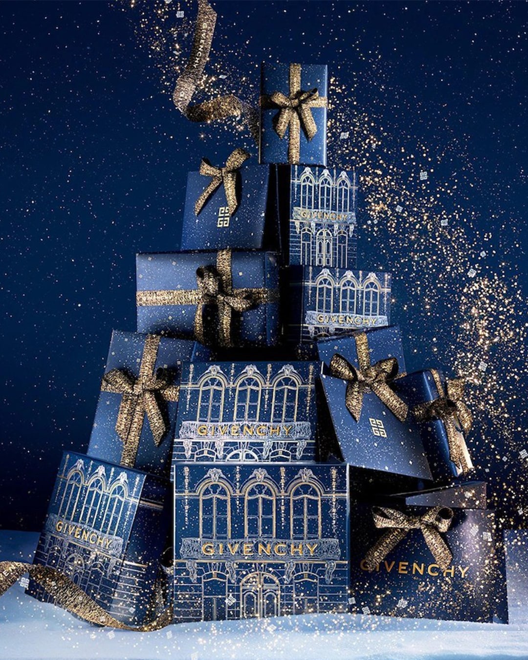 Ein festlicher Turm aus marineblauen Givenchy-Geschenkboxen, geschmückt mit goldenen Schleifen und schimmerndem Glitzer.