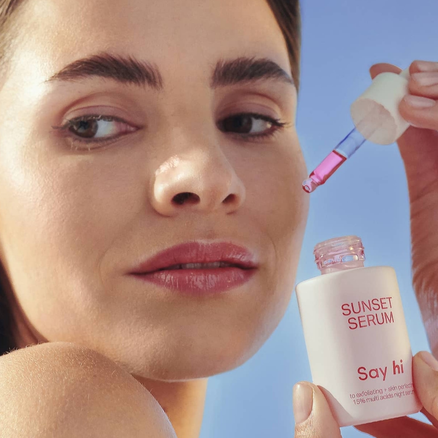 Kobieta trzyma butelkę serum Sunset z pipetą, która zawiera różowy płyn, serum przeznaczone do złuszczania i upiększania skóry.