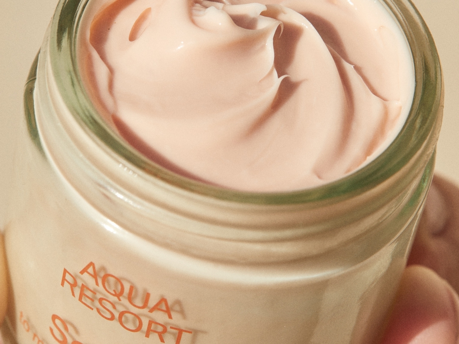 Krem Aqua Resort w szklanym słoiczku ma delikatny, brzoskwiniowy odcień i gładką konsystencję, idealny do nawilżenia skóry.