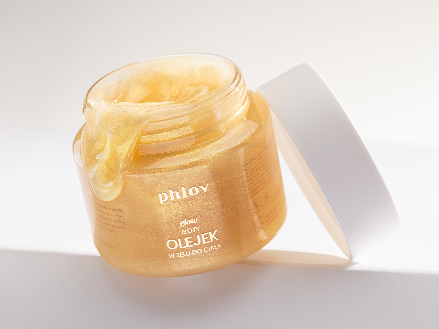 Błyszczący złoty olejek do ciała Phlov w żelu, zamknięty w przezroczystym słoiczku z białą nakrętką, idealny do pielęgnacji skóry i dodania jej blasku.