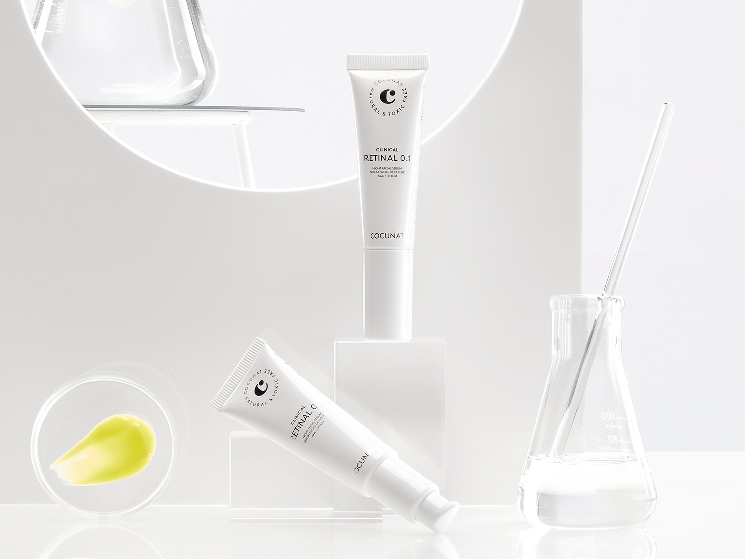 El suero facial nocturno Clinical Retinal 0.1 de Cocunat viene en un tubo blanco, presentado con un toque de suero amarillo y un vaso de precipitados transparente.