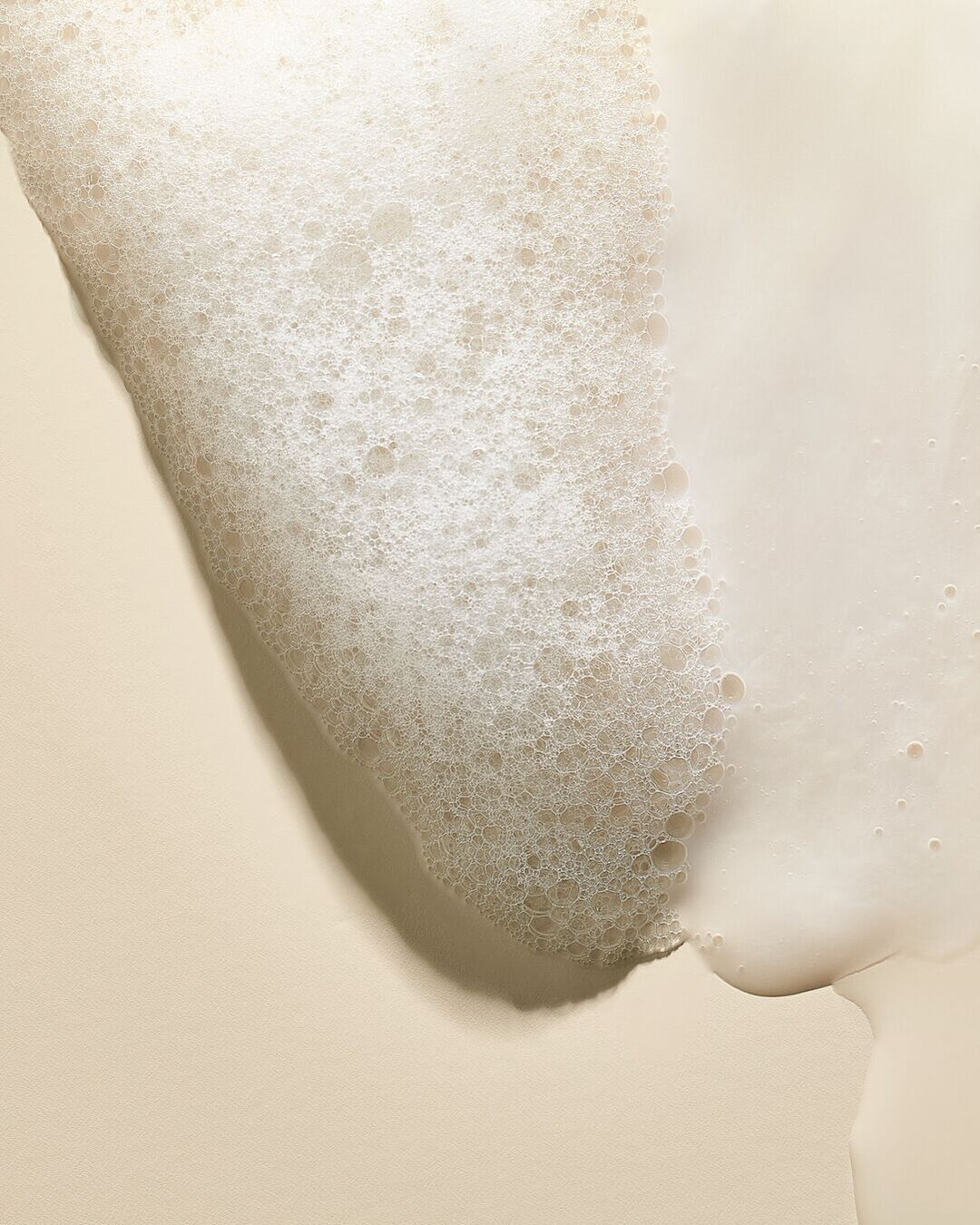 Švelnios tekstūros kreminės putos ant smėlio spalvos paviršiaus sukuria gaivumo ir švaros įspūdį.