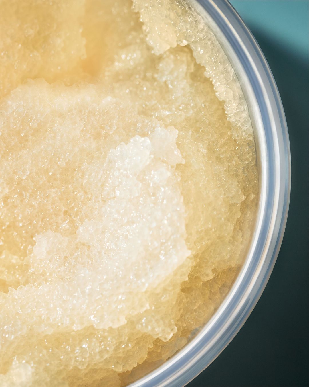 Peeling na pokožku hlavy a tělo OUAI v průhledné nádobě s žlutou květinou nahoře, s nápisem MELROSE PLACE a 8.8 oz / 250 g.