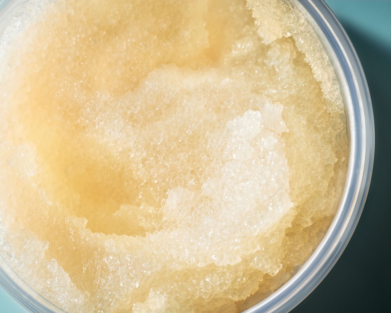 Detailní pohled na peeling s krystalickou texturou v průhledné nádobě, ideální pro jemnou exfoliaci a rozjasnění pleti.