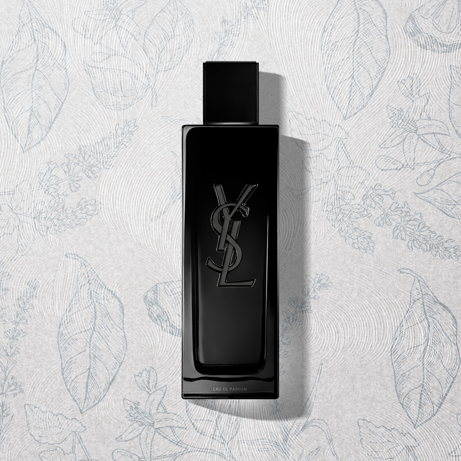 Czarny flakon perfum Yves Saint Laurent z logo YSL na tle białego papieru w delikatne kwiatowe wzory.