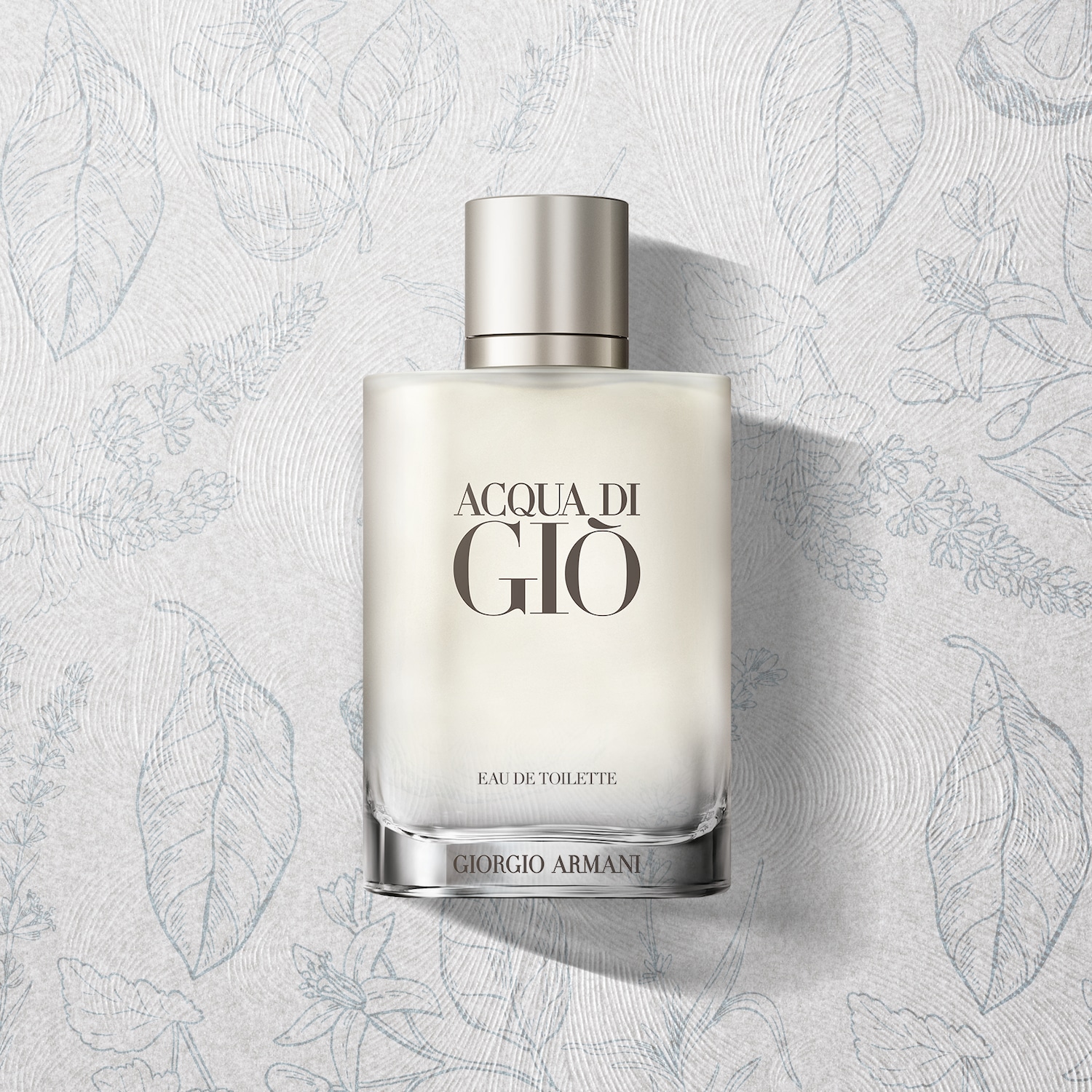 Przezroczysty flakon perfum Giorgio Armani Acqua di Giò Eau de Toilette z srebrną nakrętką na tle białego papieru w roślinne wzory.
