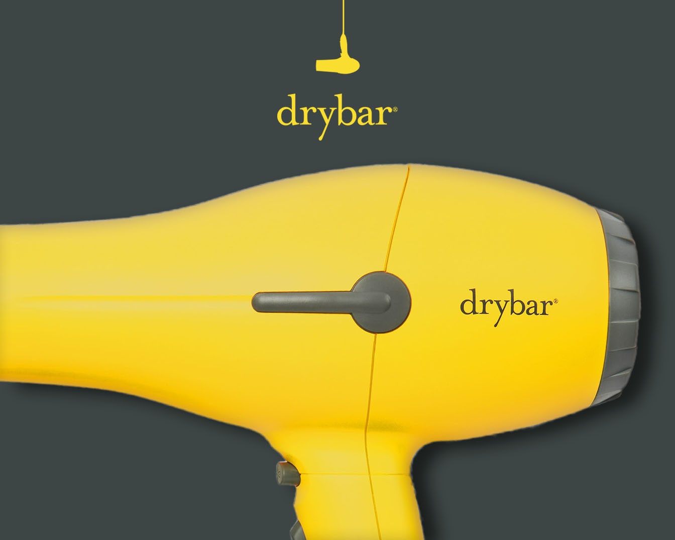 Sárga Drybar hajszárító, a márka logójával a tetején és az oldalán, szürke háttér előtt.