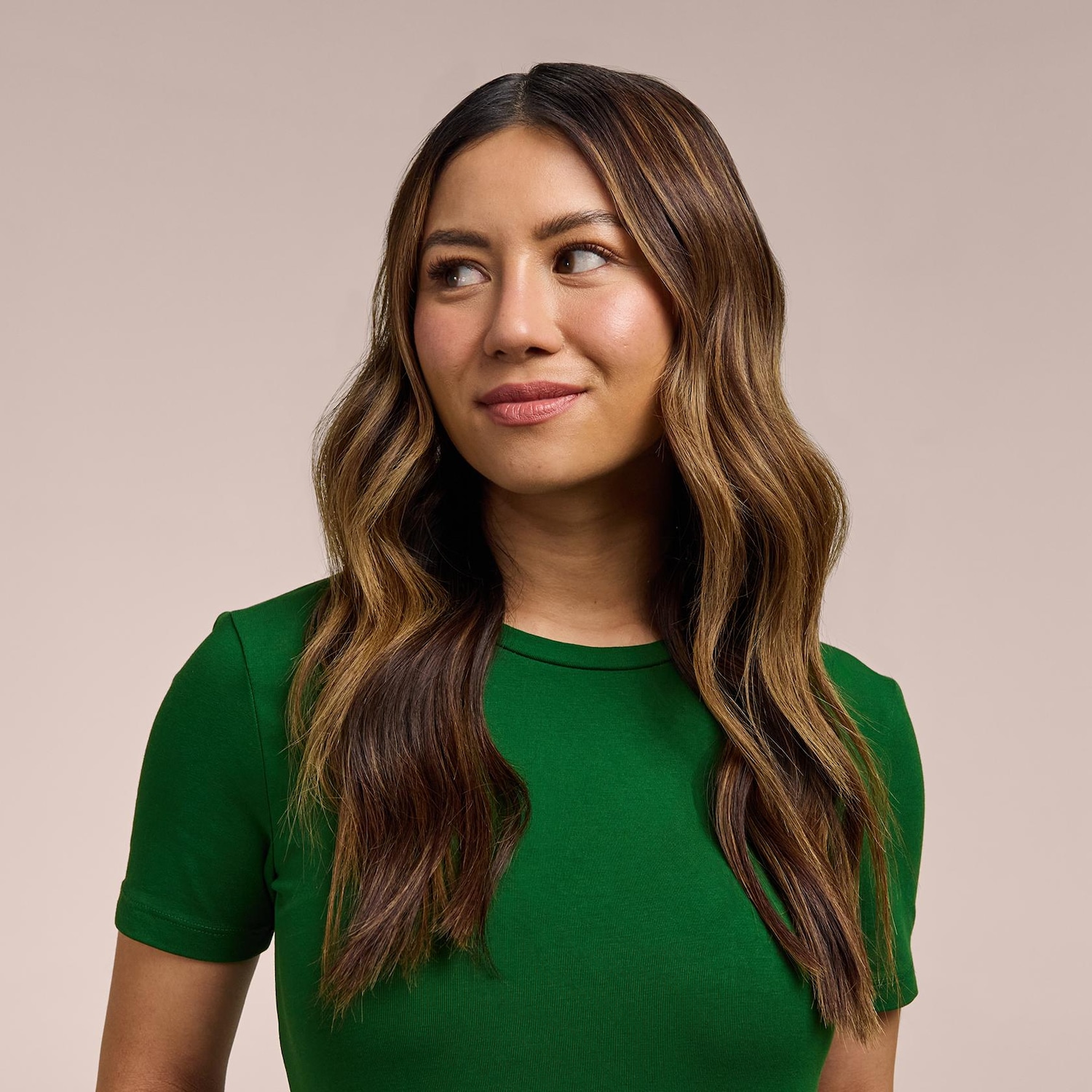 Egy zöld pólót viselő, hullámos, barna hajú nő oldalra néz, arca enyhén mosolyog.