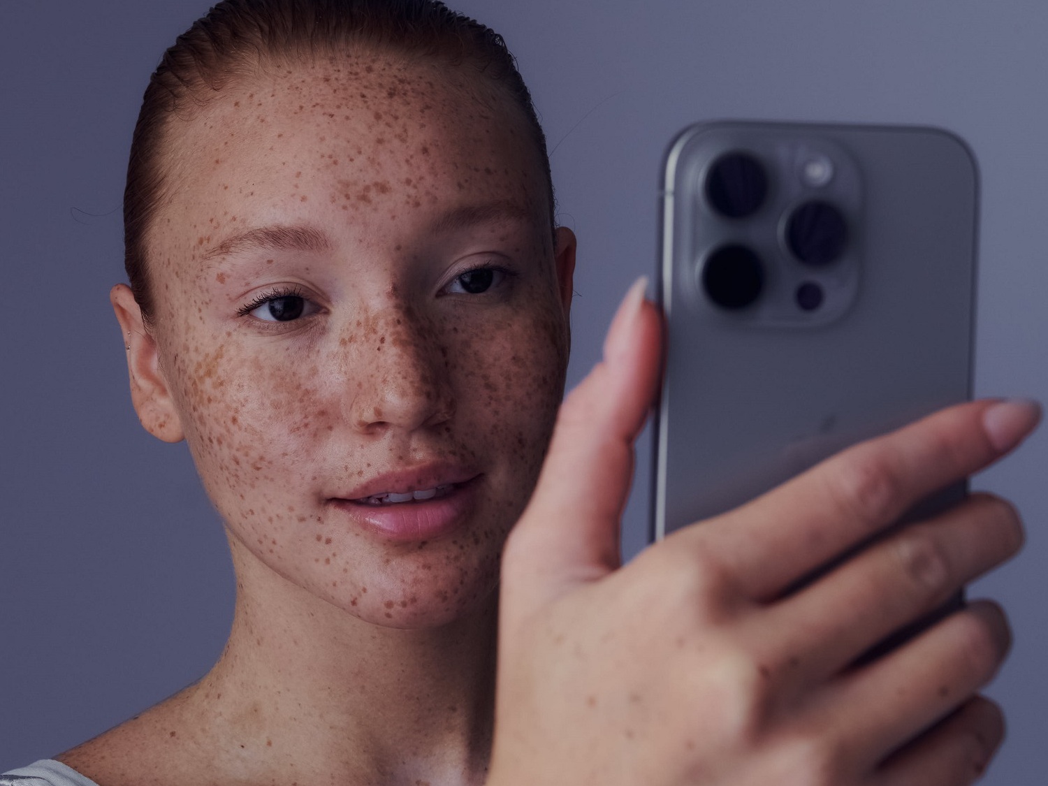 Nahaufnahme einer Frau mit Sommersprossen, die ein graues Smartphone hält und ein Selfie macht.