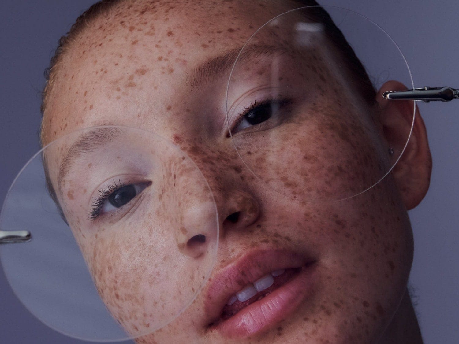 Nahaufnahme eines Frauengesichts mit Sommersprossen, wobei transparente Kreise vor einem Auge gehalten werden, um die Haut zu betonen.