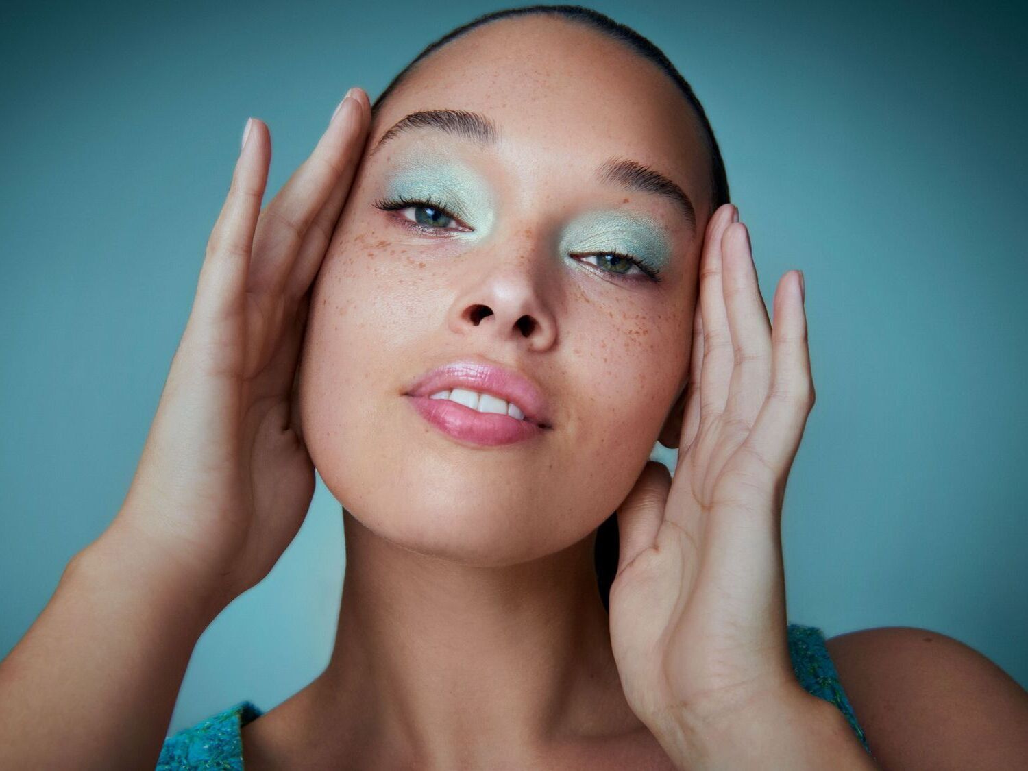 Šviesiaplaukė moteris su šviesiai žaliais akių šešėliais ir natūraliu makiažu pozuoja su „Douglas Beauty Card“ reklama.