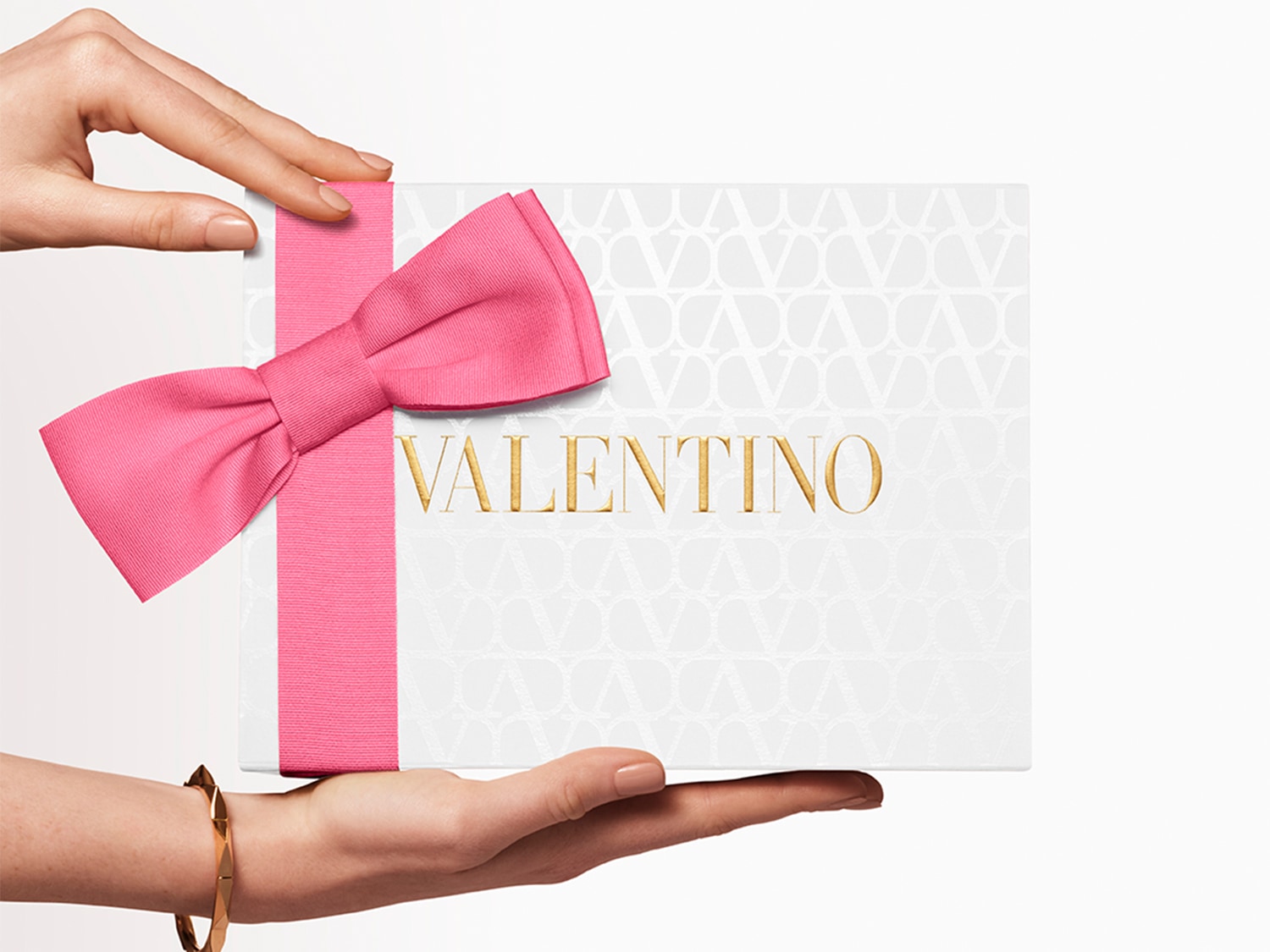 Voici un coffret Valentino blanc, orné d'un ruban rose vif et d'un nœud assorti, présenté délicatement dans les mains.
