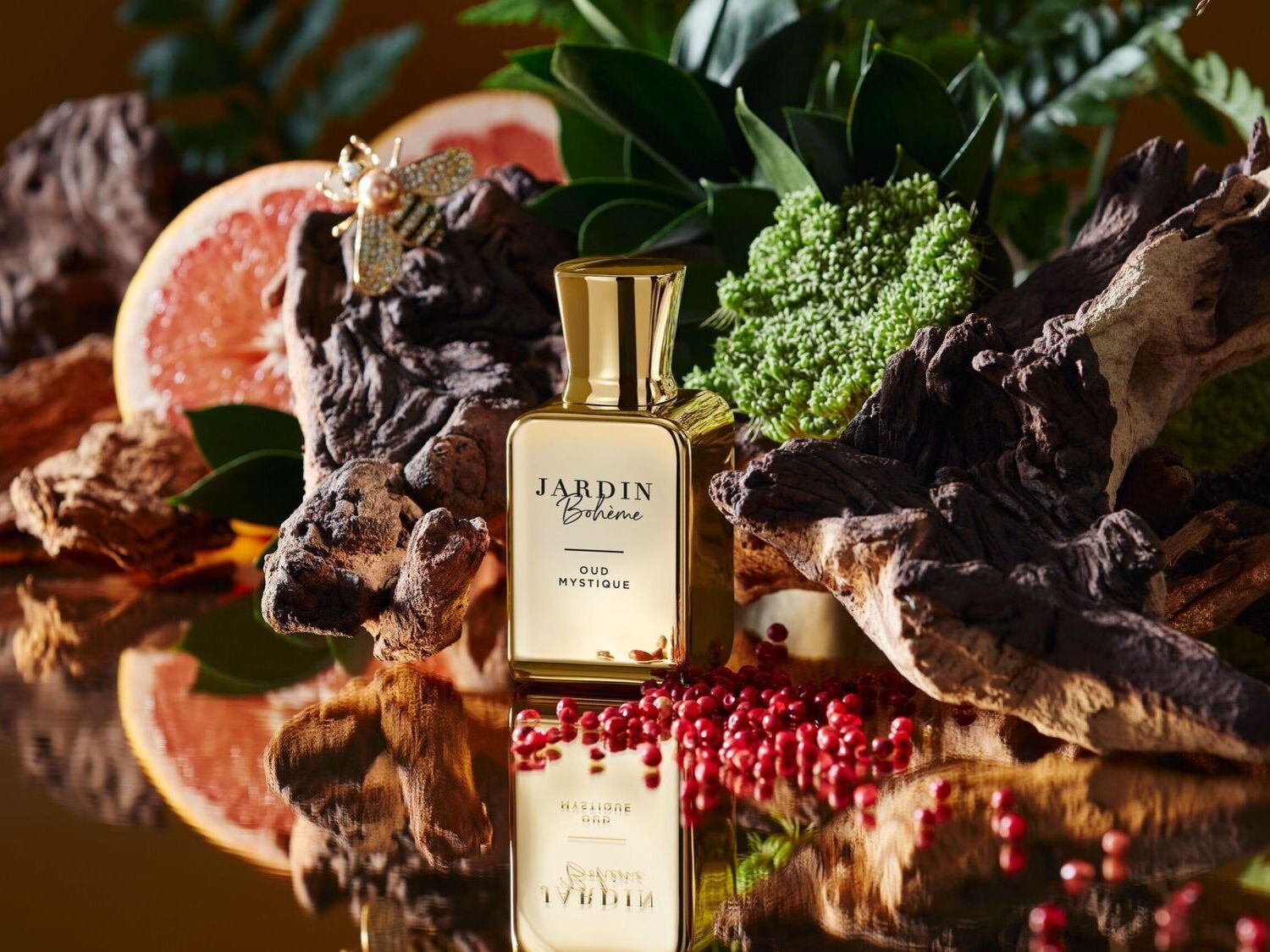 Auksinis „Jardin Bohème Oud Mystique“ buteliukas, apsuptas gamtos elementų, tokių kaip mediena, žaluma ir raudonos uogos, atspindi prabangų ir natūralų kvapą.