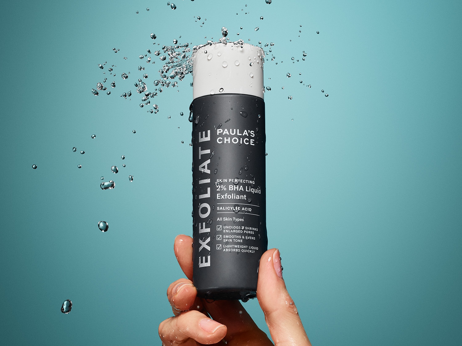 Paula's Choice Skin Perfecting 2% BHA Liquid Exfoliant in einer grauen Flasche mit weißer Kappe, umgeben von Wassertropfen, die eine leichte, schnell einziehende Flüssigkeit für alle Hauttypen verspricht.