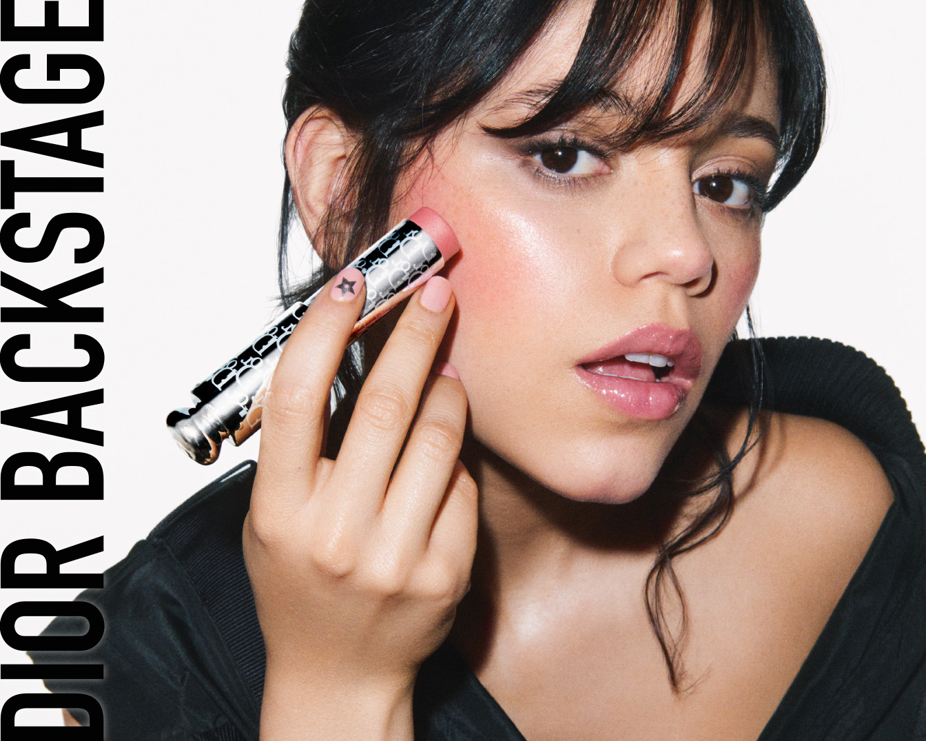 Une femme applique un blush rose de Dior Backstage sur sa joue, le packaging argenté et noir du stick est visible.