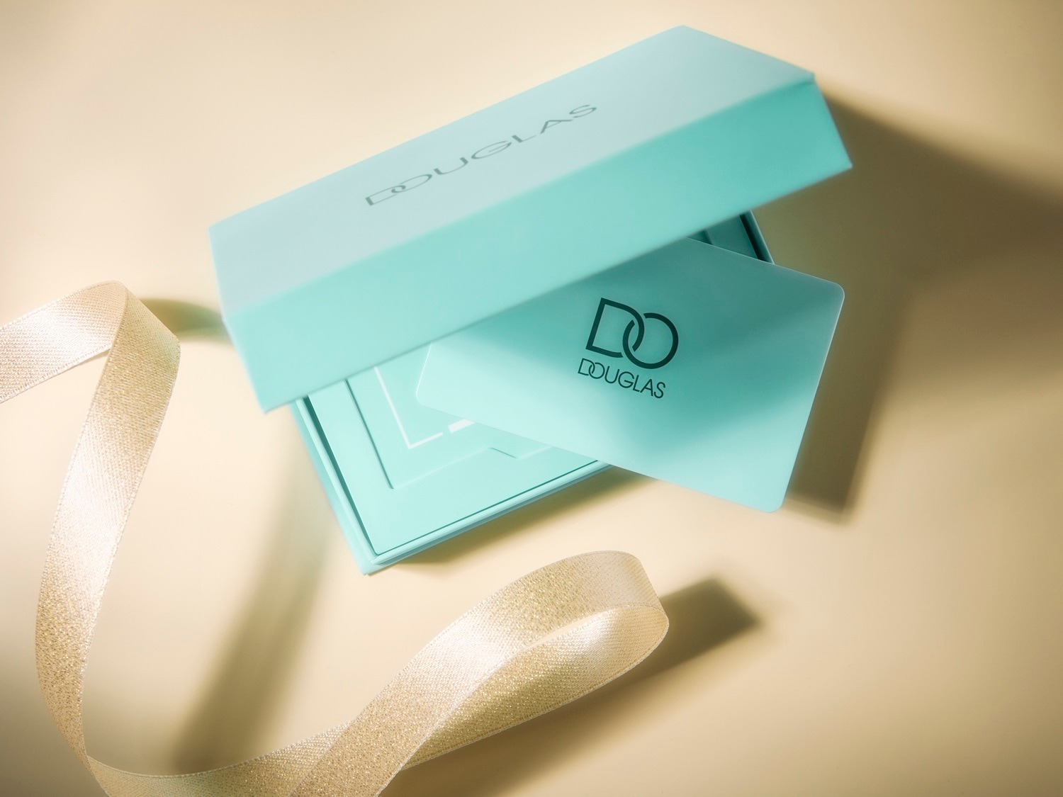 Elegancki zestaw upominkowy Douglas w turkusowym pudełku z kartą podarunkową i złotą wstążką, idealny na prezent.