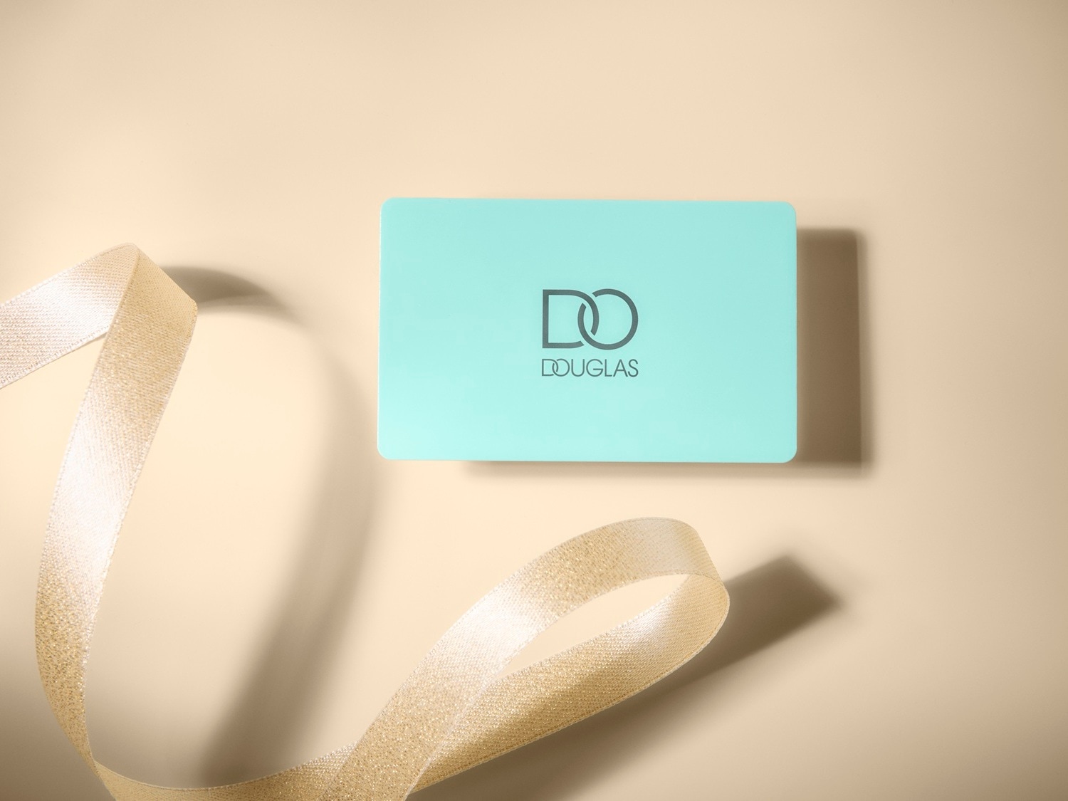 Jasnoniebieska karta podarunkowa Douglas z logo DO na beżowym tle, ozdobiona złotą wstążką, idealna na prezent.