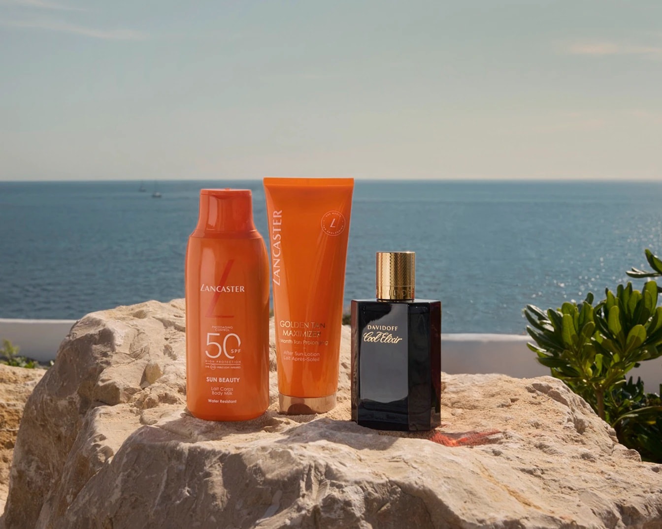 Sulla roccia, flacone arancione di latte corpo Lancaster Sun Beauty SPF 50, tubo Lancaster Golden Tan Maximizer e flacone nero di Davidoff Cool Elixir.