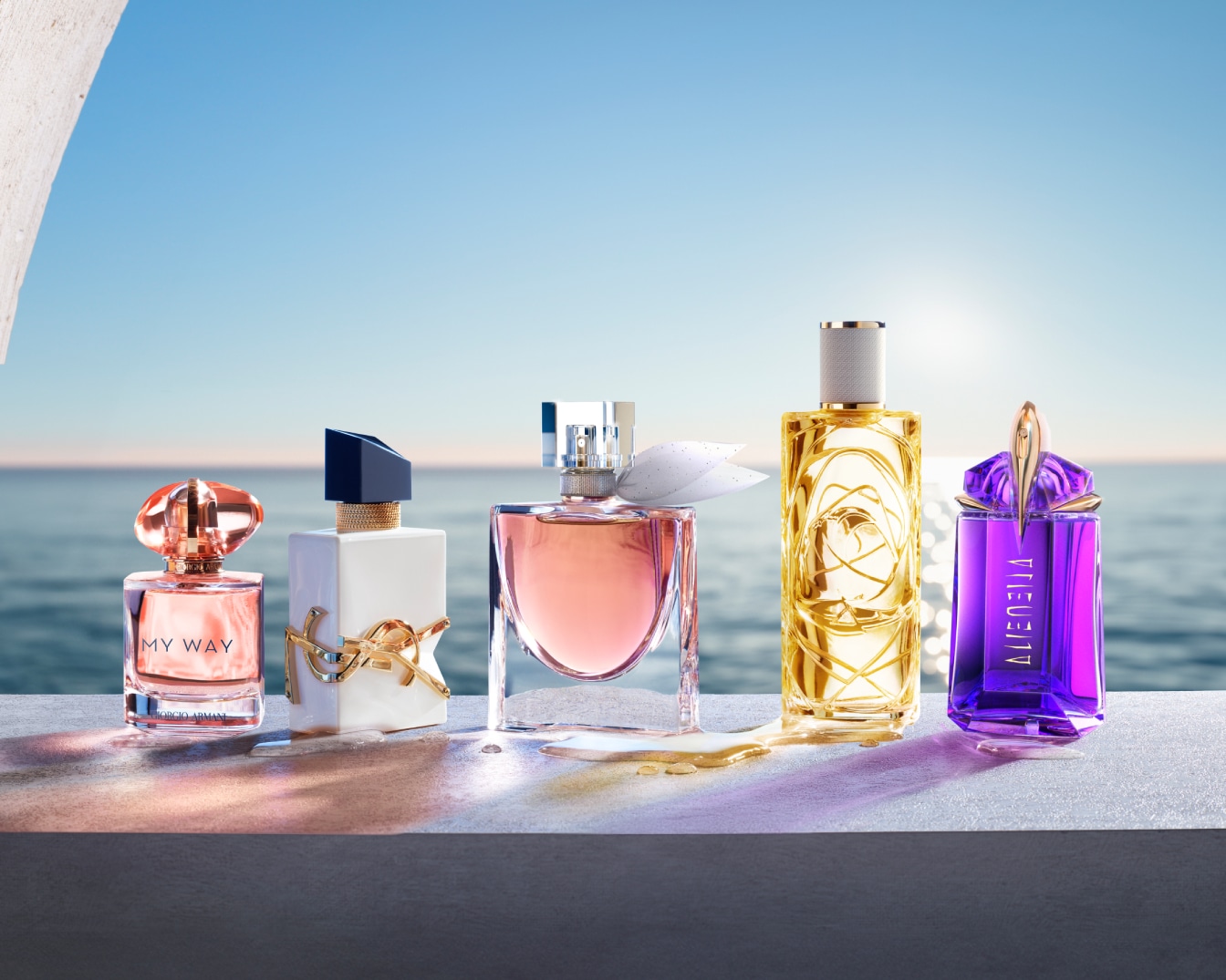 Eine Reihe von Parfümflaschen verschiedener Marken und Formen stehen vor einem verschwommenen Hintergrund aus Meer und Himmel, der einen Hauch von Luxus und Sommerfrische vermittelt.