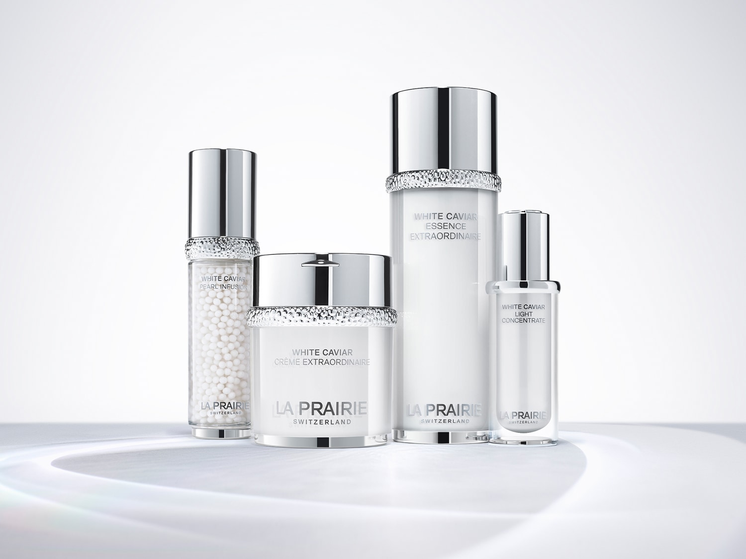 Découvrez la collection White Caviar de La Prairie, comprenant Pearl Infusion, Crème Extraordinaire, Essence Extraordinaire et Light Concentrate, présentés dans des emballages blancs et argentés élégants.