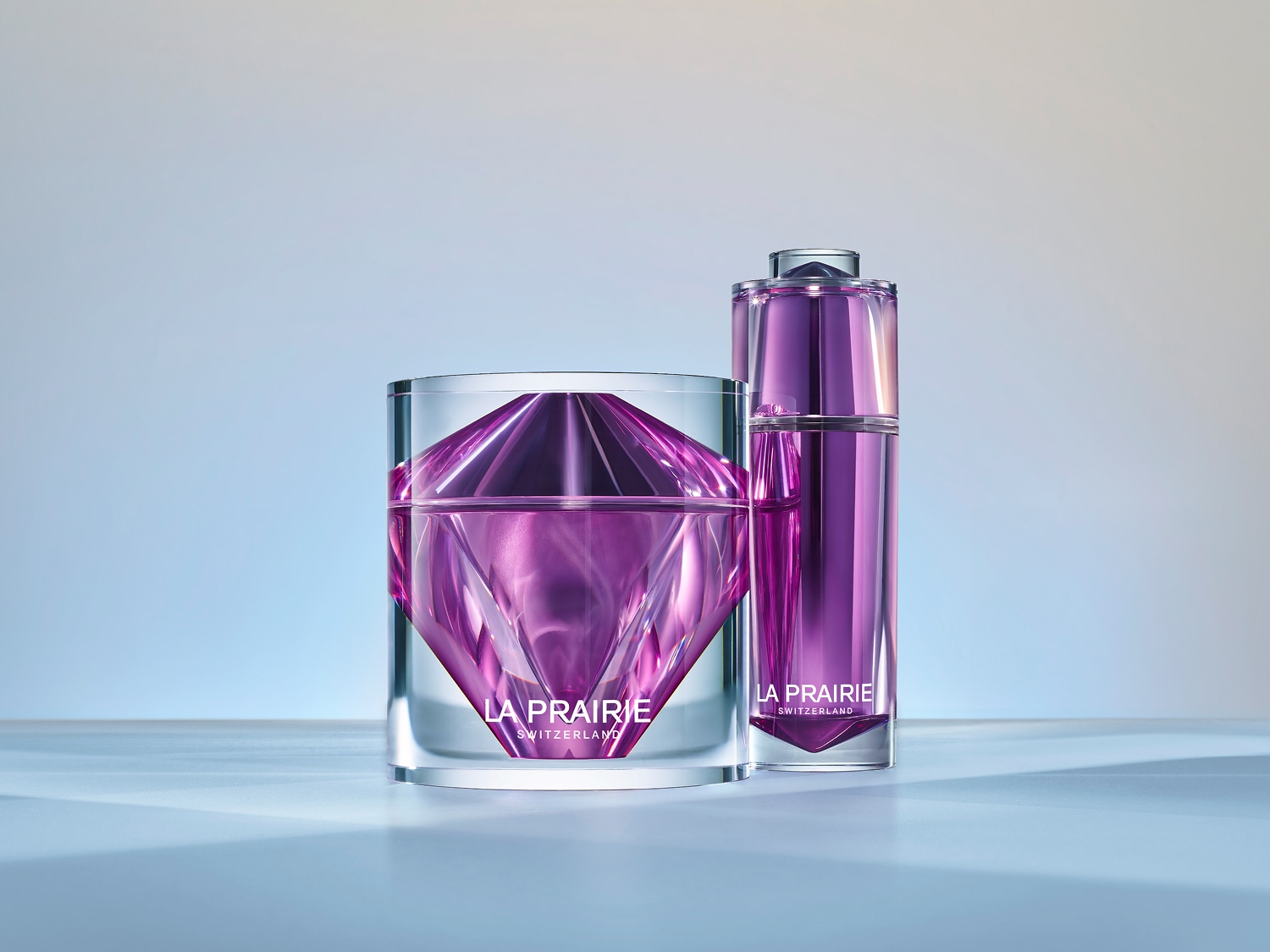 Découvrez le luxe suisse avec La Prairie : un pot en verre transparent révèle une crème violette taillée comme un diamant, accompagné d'un flacon élégant assorti.