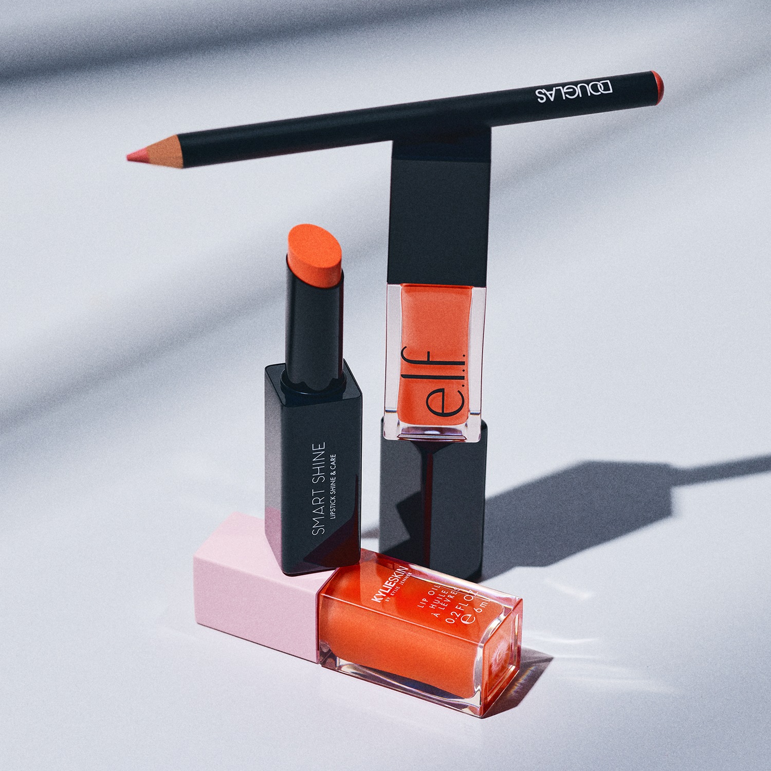 Verschillende make-upproducten voor de lippen, waaronder een Douglas lipliner, een Smart Shine lipstick, een Elf lipgloss en een Kylie Skin lipolie, allemaal in levendige oranje tinten.
