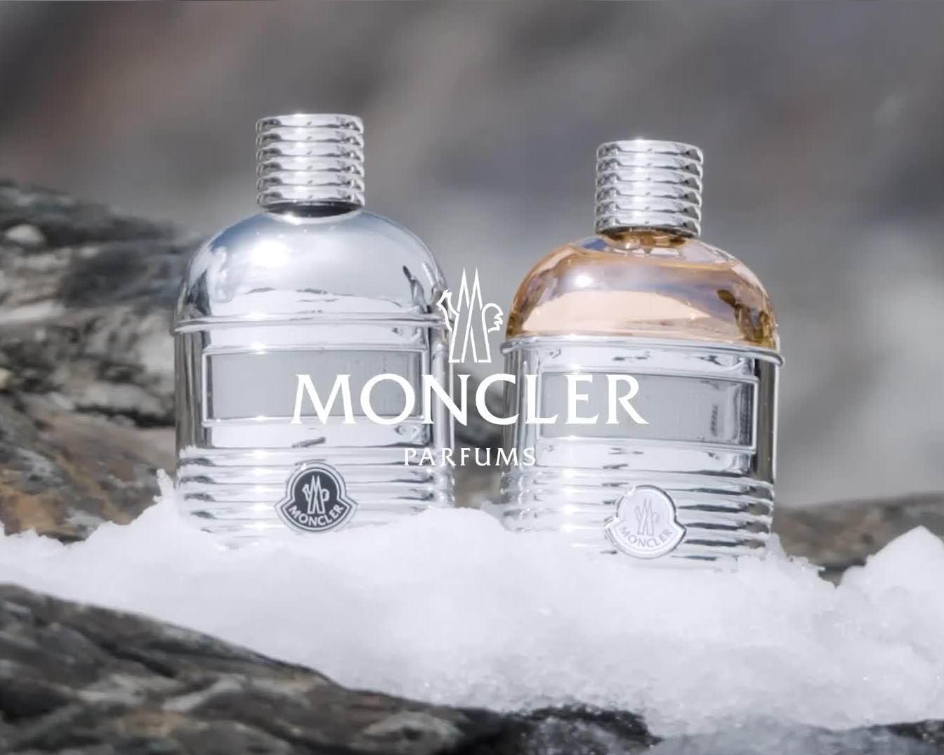 Dwa flakony perfum Moncler, jeden srebrny, drugi złoty, stoją na śniegu, prezentując luksus i elegancję.