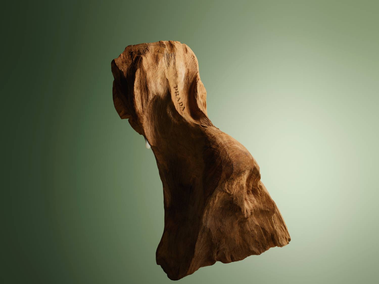 Detailný záber na drevenú sochu s vyrytým nápisom PRADA na zelenom pozadí.