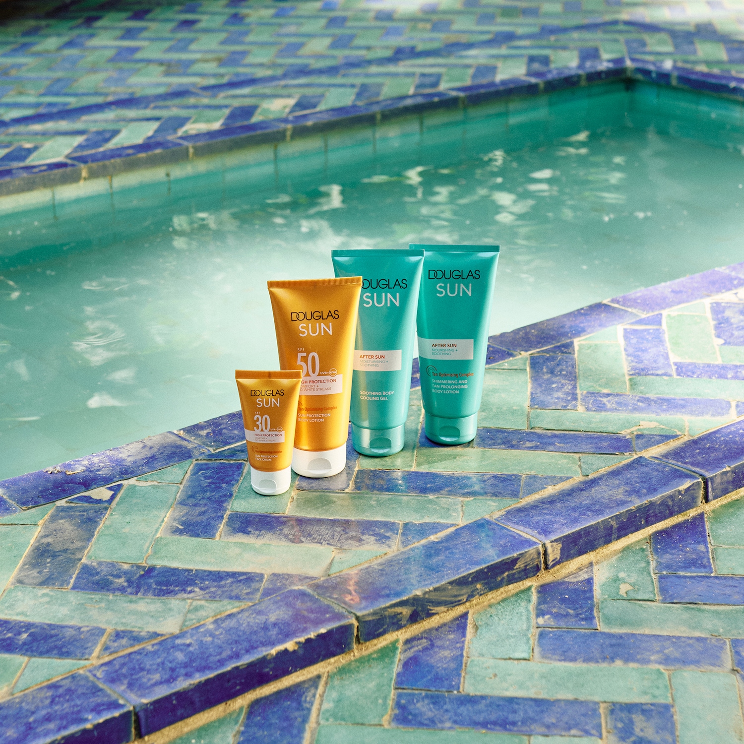 Une collection de produits solaires Douglas Sun, comprenant des lotions de protection solaire SPF 30 et 50 en tubes orange, ainsi que des lotions après-soleil en tubes turquoise, présentés près d'une piscine.