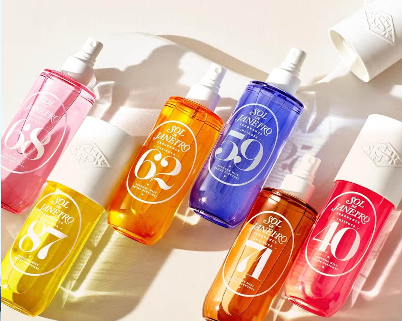 Kolorowe mgiełki zapachowe Sol de Janeiro Cheirosa w odcieniach różu, żółci, pomarańczy, fioletu i czerwieni, każda z białą nakrętką i dużym numerem na opakowaniu.
