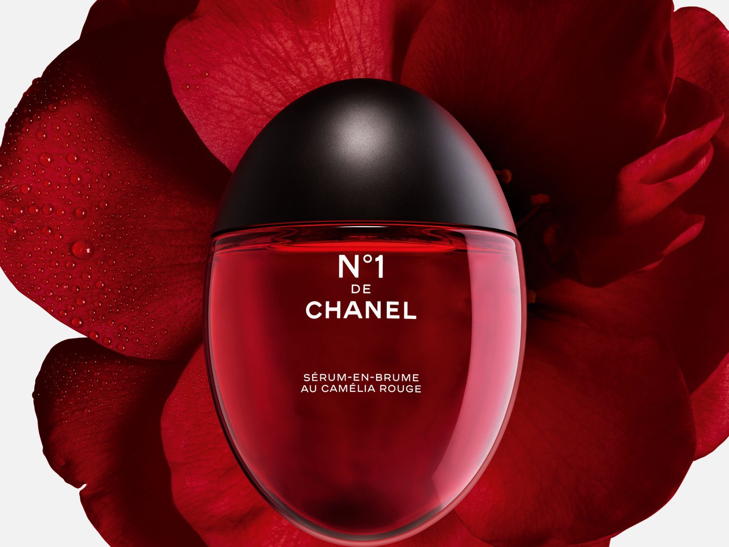 Roter Chanel N°1 Serum-En-Brume Flakon mit schwarzem Deckel, umgeben von einer roten Kamelienblüte.