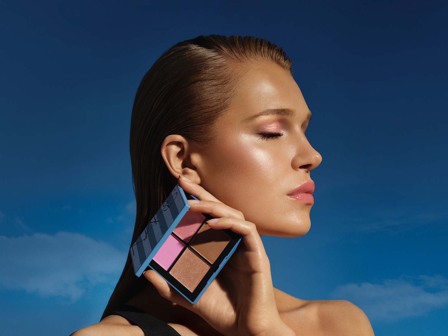 Nahaufnahme einer Frau mit glatter Haut und rosa Lidschatten, die eine hellblaue NARS-Palette mit vier Farben in Rosa- und Brauntönen hält.