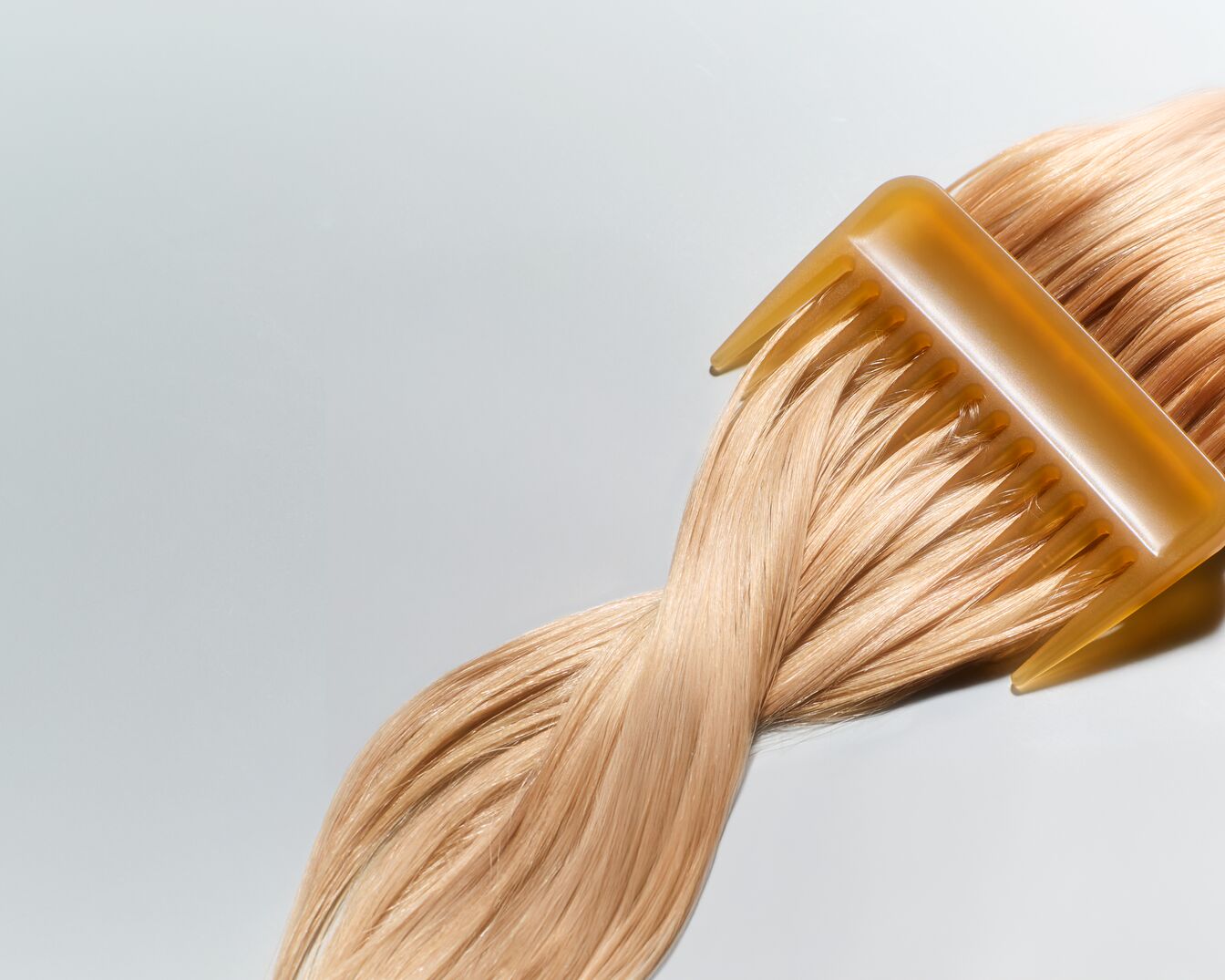 Een blonde haarlok wordt gekamd met een amberkleurige kam, wat de gladde textuur en glans van het haar benadrukt.