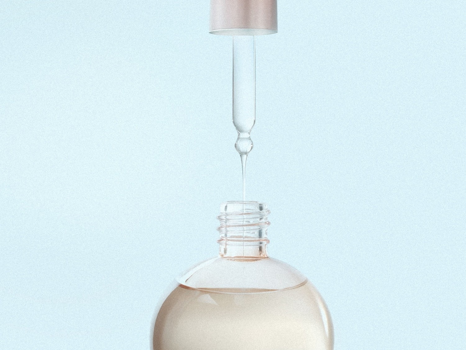 Close-up van een heldere serumfles met een glazen pipet die een druppel serum afgeeft, tegen een zachtblauwe achtergrond.