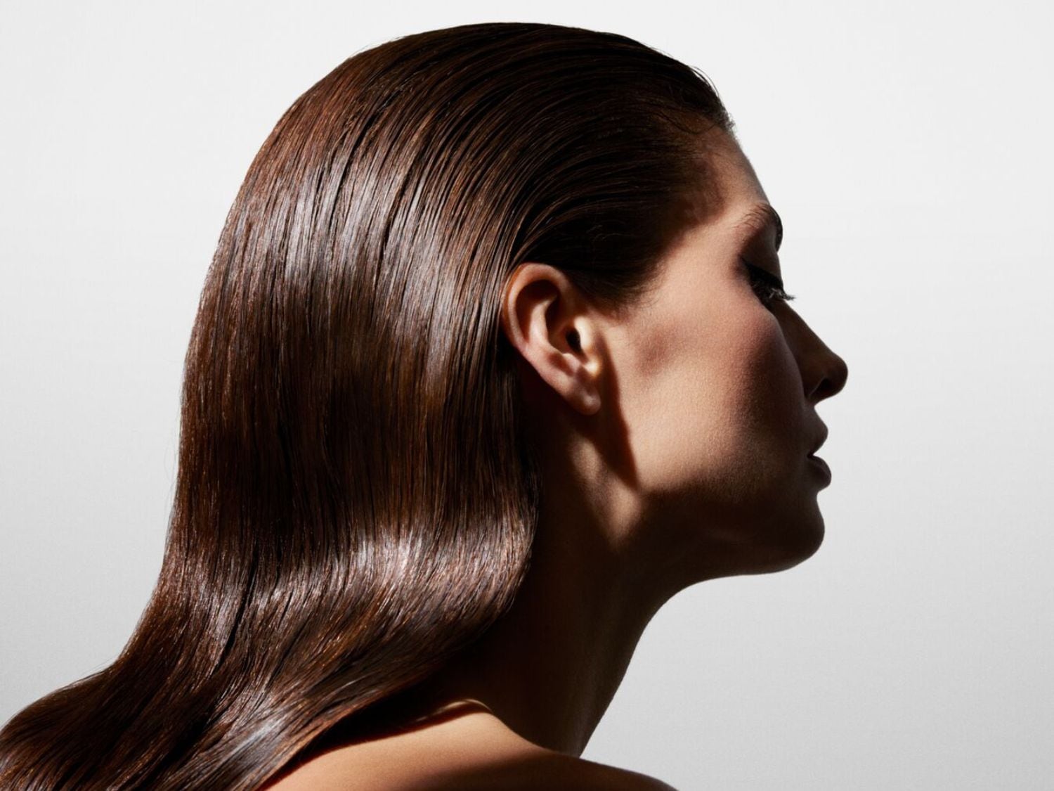 Profilból látható nő, sötétbarna, fényes, hátrafésült hajjal, a háttér fehér.