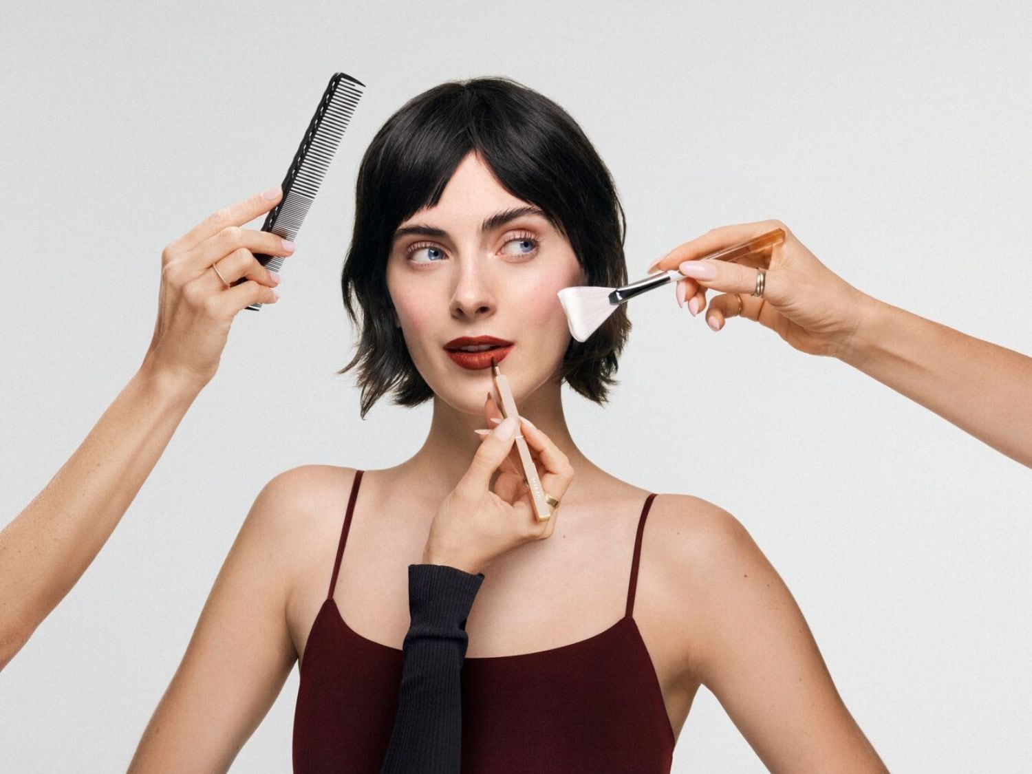 Egy nő sminkelése közben látható, ahogy egy fésűvel fésülik a haját, egy ecsettel az arcát festik, és egy ceruzával a száját színezik.