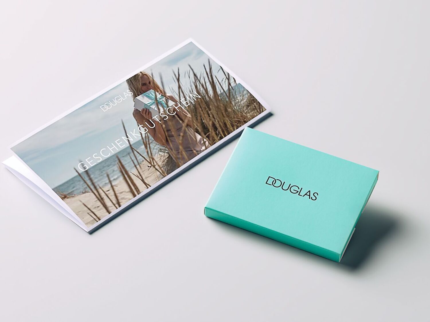 Découvrez l'élégance avec le coffret cadeau turquoise Douglas, accompagné d'une carte cadeau mettant en scène une femme sur la plage, le cadeau parfait pour toutes les occasions.