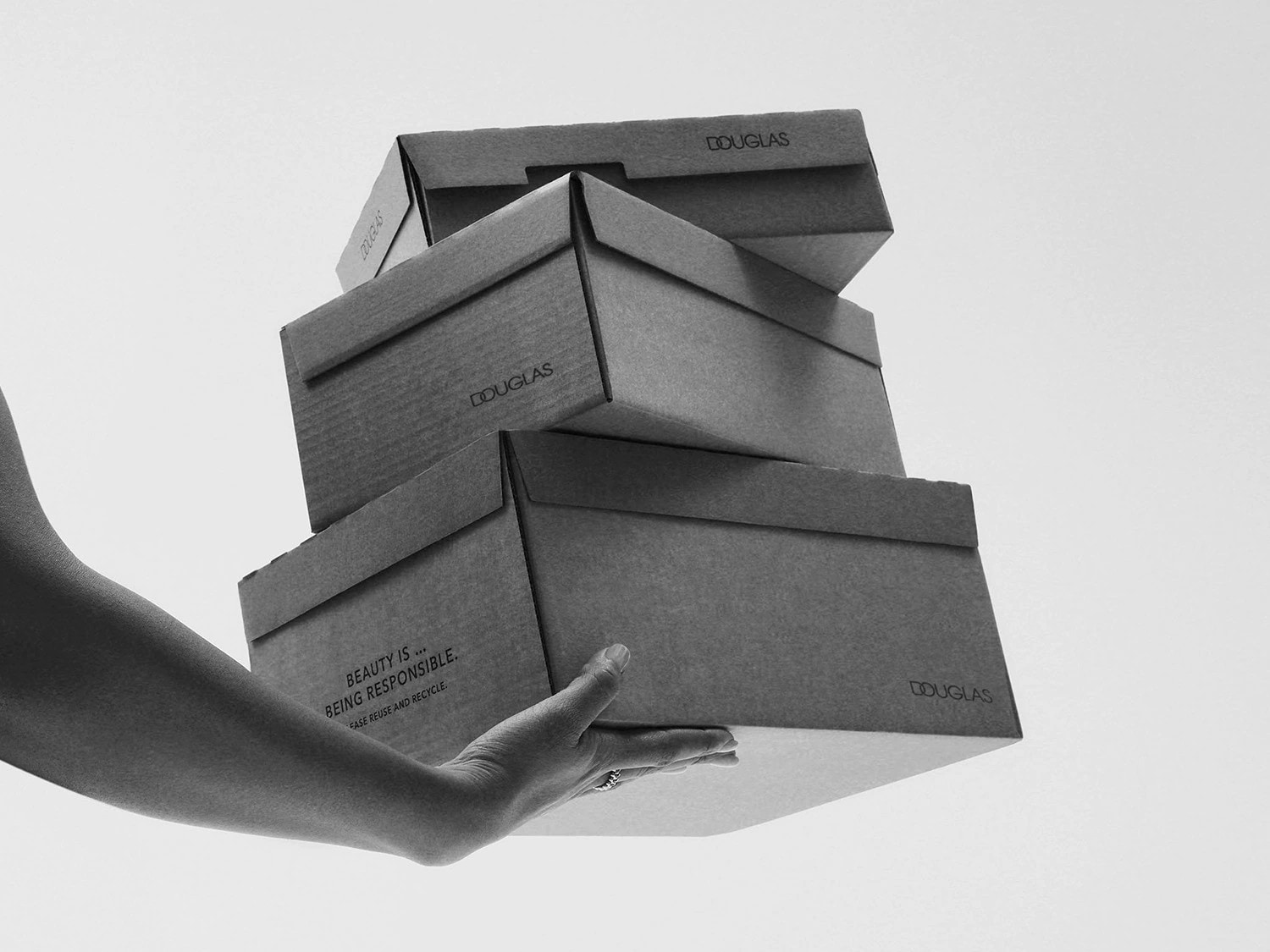 Eine Hand hält einen Stapel Douglas-Kartons, auf denen steht: "Schönheit bedeutet, verantwortungsbewusst zu sein. Wiederverwenden und recyceln".