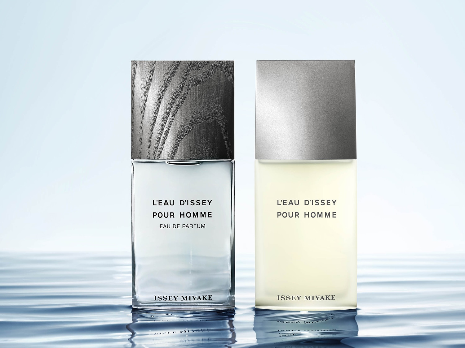 Zwei Flakons L'Eau d'Issey Pour Homme Eau de Parfum, einer mit holzgemusterter Kappe und bläulichem Inhalt, der andere mit silberner Kappe und beigem Inhalt, beide auf einer Wasseroberfläche.