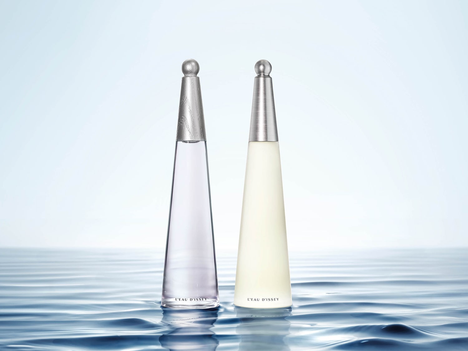 Zwei Flakons L'EAU D'ISSEY Eau de Toilette, der eine mit durchsichtigem Flakon und silberfarbenem Verschluss, der andere mit undurchsichtigem, cremefarbenem Flakon und silberfarbenem Verschluss, stehen auf einer Wasseroberfläche.