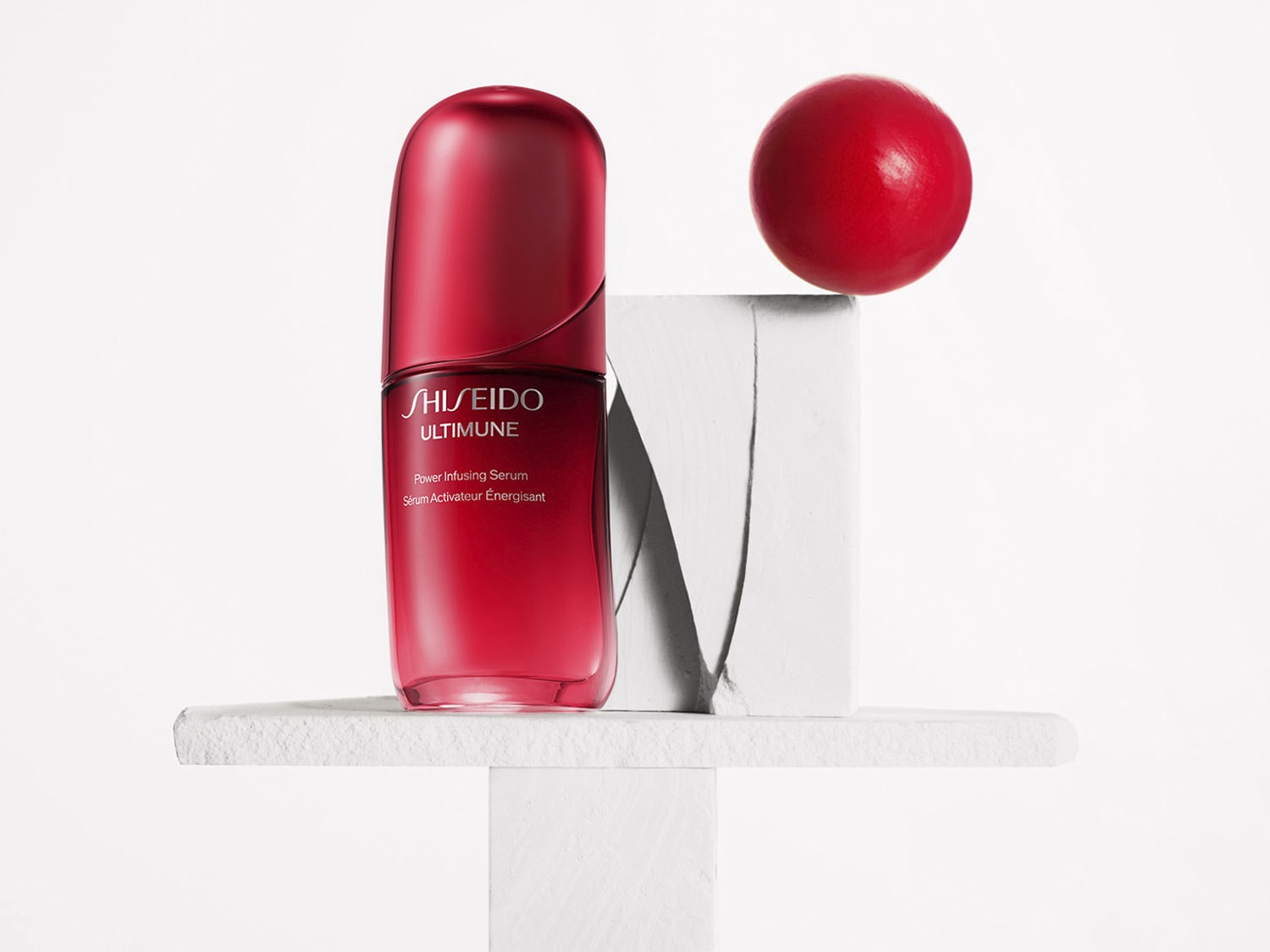 A Shiseido Ultimune Power Infusing Serum piros színű üvegben, fehér alapon helyezkedik el, mellette egy piros gömb látható.