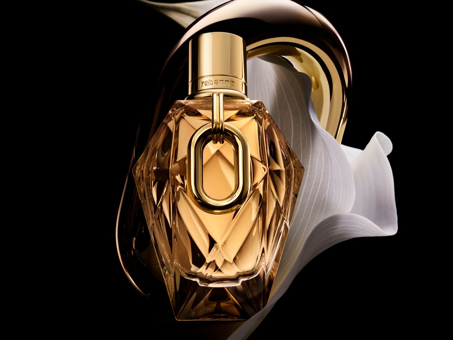 A Rabanne átlátszó, arany színű, sokszögletű üvegben lévő parfüm, arany kupakkal és virágokkal a háttérben, luxust és kifinomultságot sugároz.