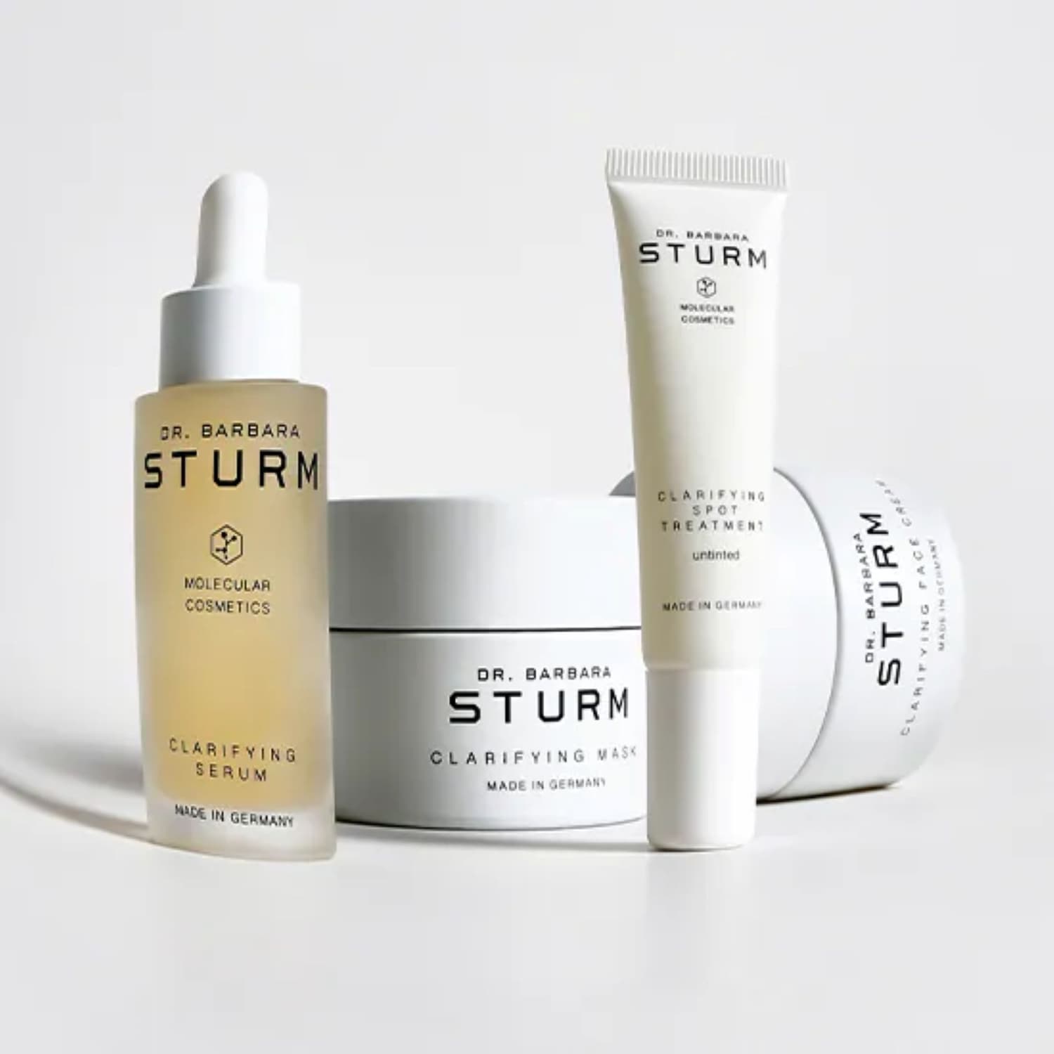 Dr. Barbara Sturm's Hautpflegeprodukte in weißen Verpackungen, darunter ein klärendes Serum, eine Maske, eine Spot-Behandlung und eine Gesichtscreme.