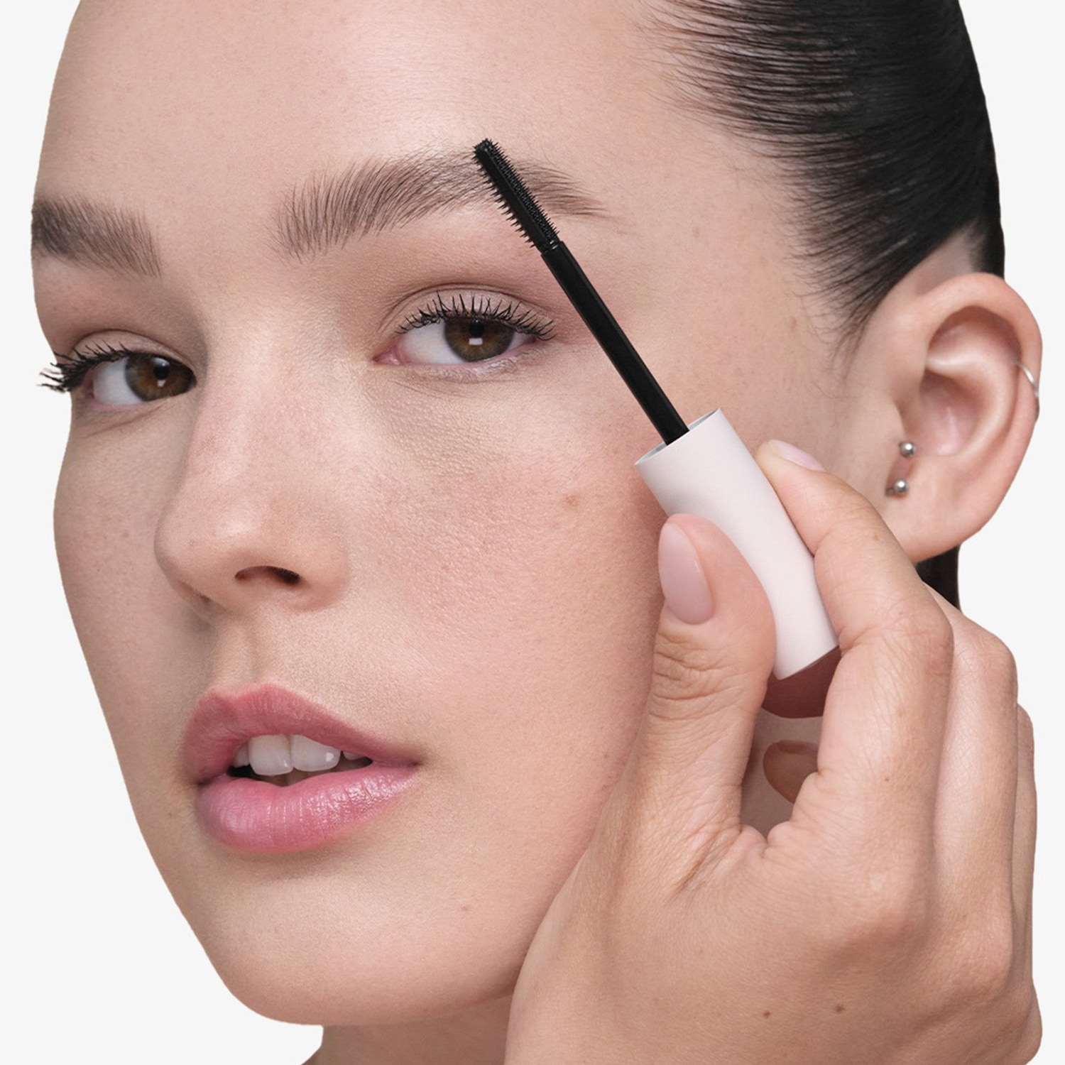 Une femme utilise une brosse à sourcils noire avec un manche blanc pour coiffer ses sourcils, mettant en valeur leur forme et leur définition.