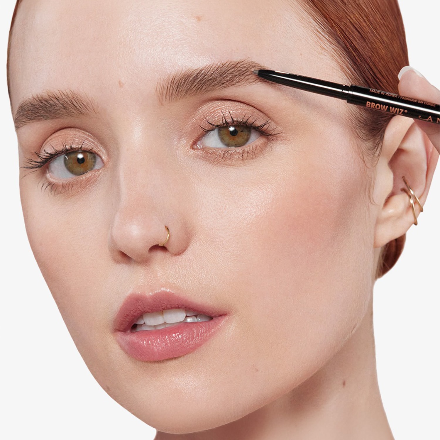 Gros plan sur une femme utilisant un crayon noir Brow Wiz pour définir ses sourcils, mettant en valeur la précision et la couleur naturelle du produit.