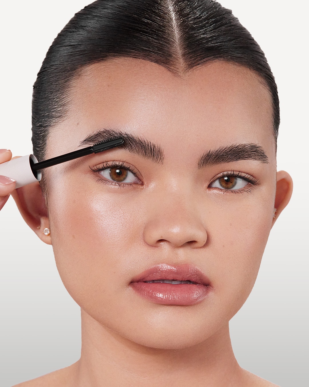 Une femme se brosse les sourcils avec une brosse à mascara noire et blanche pour un look soigné.