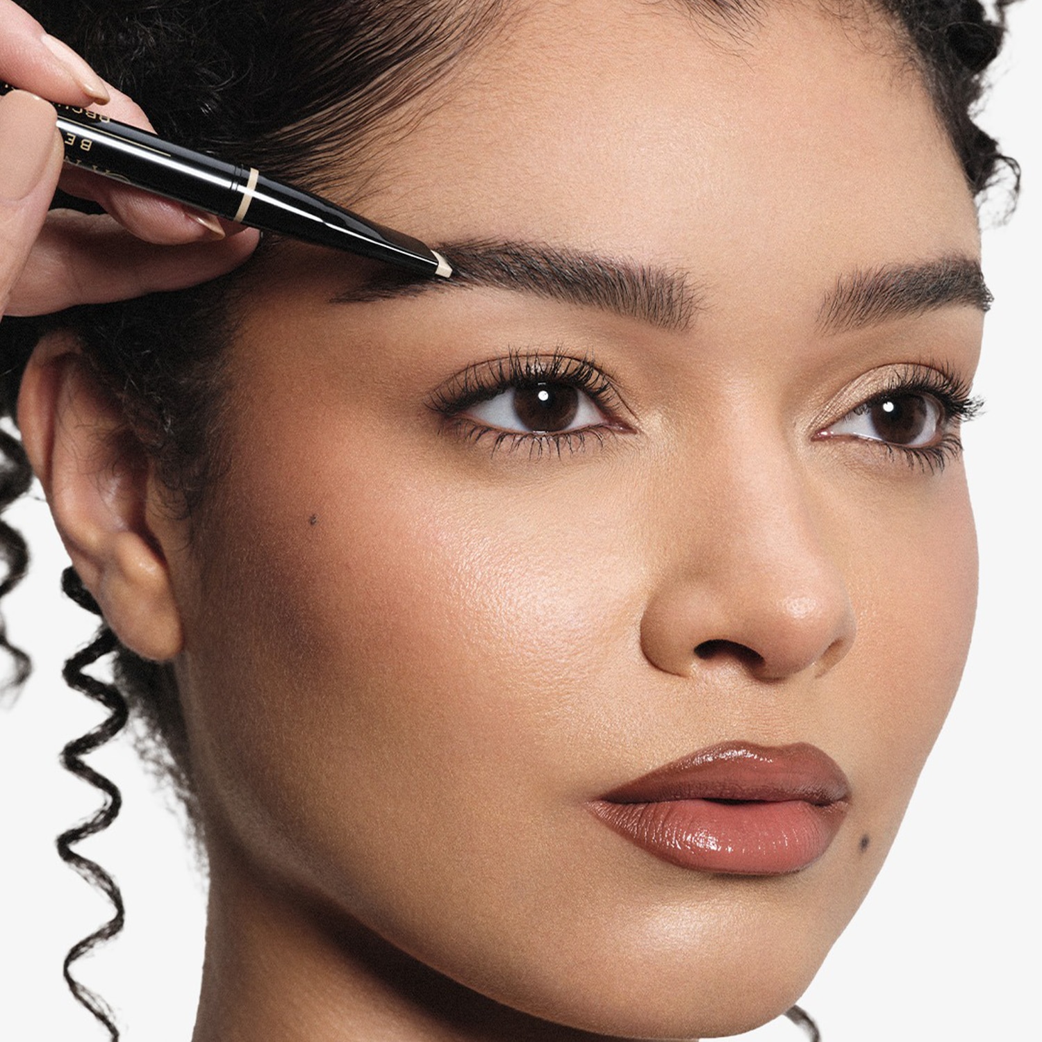 Une femme utilise un crayon à sourcils noir pour définir ses sourcils, mettant en valeur son regard.