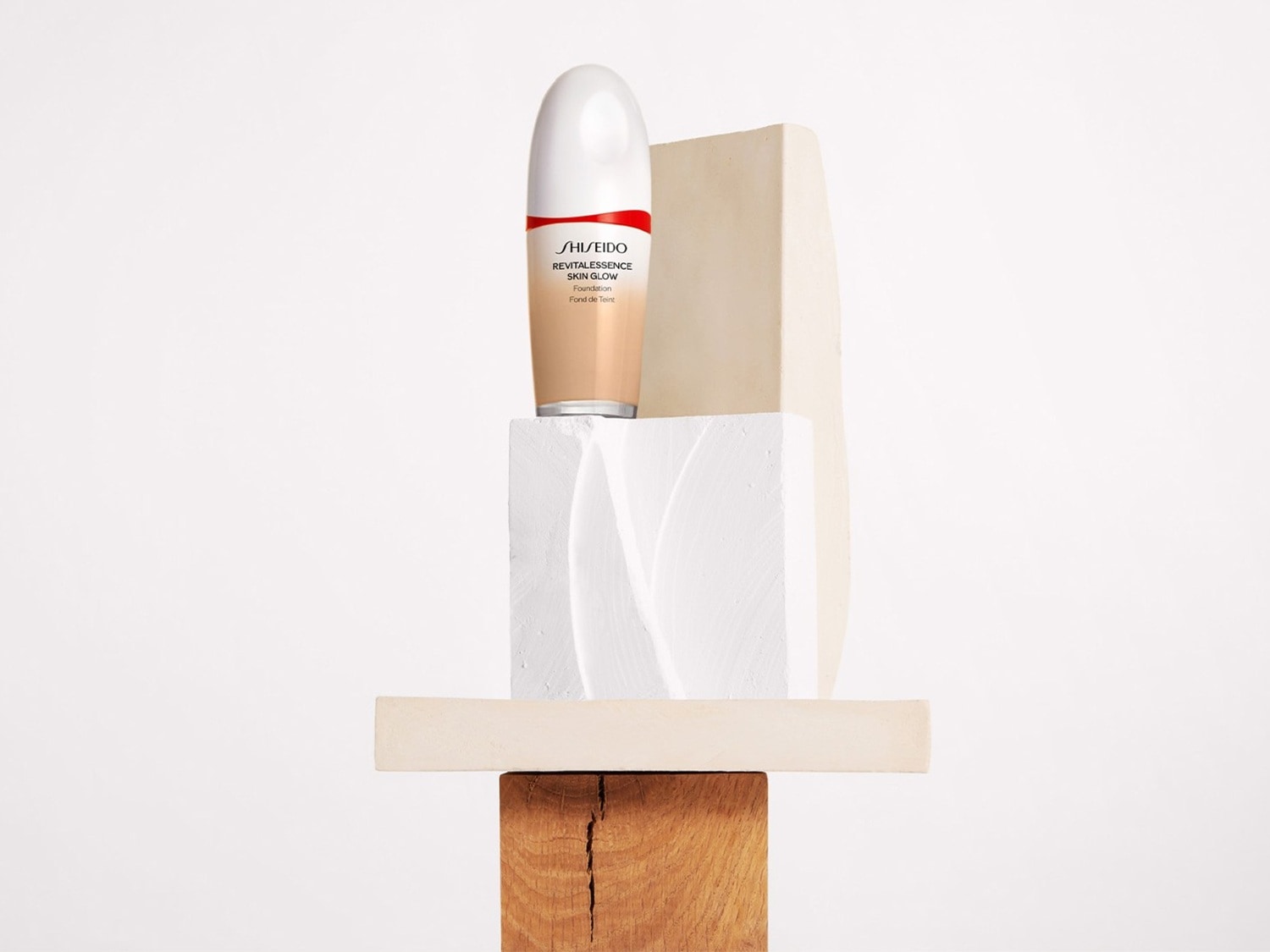 Buteleczka podkładu Shiseido Revitalessence Skin Glow w odcieniu beżowym, umieszczona na abstrakcyjnej kompozycji z drewnianych i betonowych bloków.