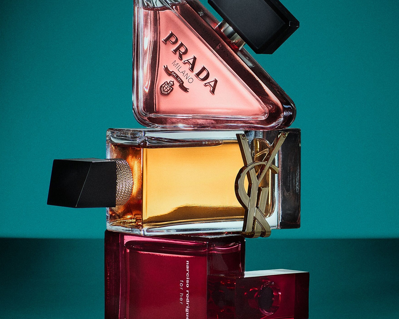 Trois parfums de marques différentes sont empilés les uns sur les autres : Prada rose, Yves Saint Laurent doré et Narciso Rodriguez rouge.
